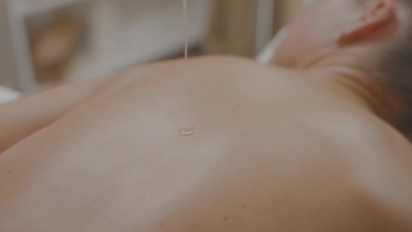 Pouring Massage Oil From Bowl Onto Woman Back in Spa Room on Massage Table