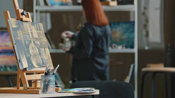 Abstract Painting Black Canvas with Gold Drawings on Easel Stands on Table in Workshop Studio with