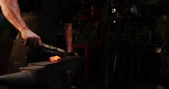 Mid-section of blacksmith using wire brush on hot iron