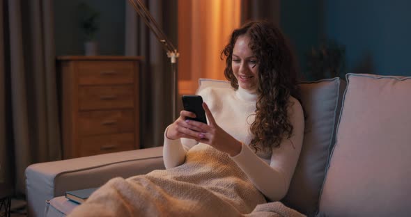 A Girl Sits on Couch in Evening By Light of Lamp Legs on the Coffee