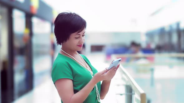 Brunette Woman Uses Mobile Phone in Business Center and Smiles