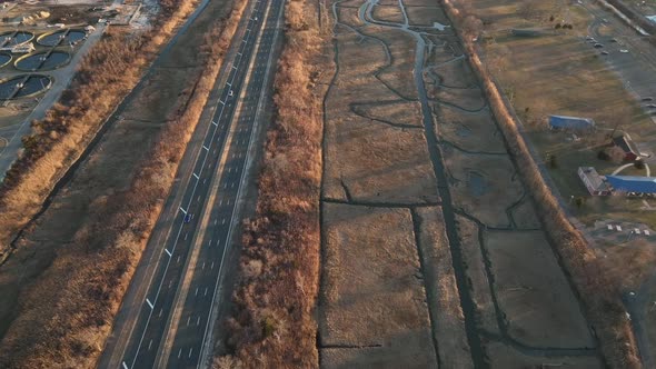 An aerial view high over a marsh on Long Island, NY. A long road with a few cars run next to it, sho