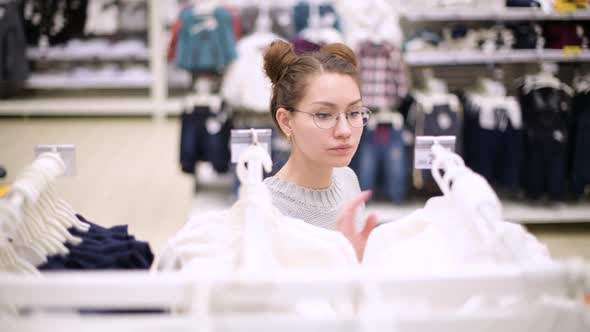 a young mother walks along a row of children's clothes, choosing a sweater for her child