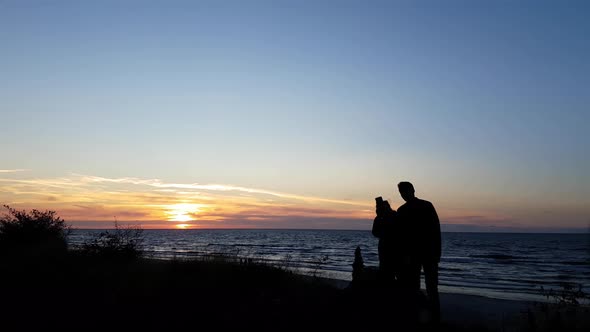 Young couple watching sunset on the beach. Only silhouettes visible. Colorful sunset. Man and woman