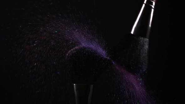 Makeup Brushes with Pink and Purple Flying Eye Shadow Powder Particles on Black