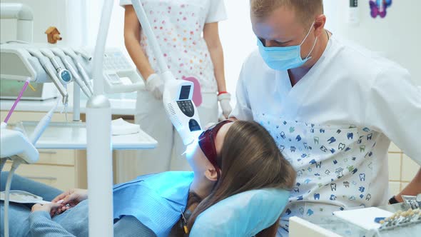 Laser teeth whitening in a dental clinic. A dentist in a white coat treats a girl in UV-protective