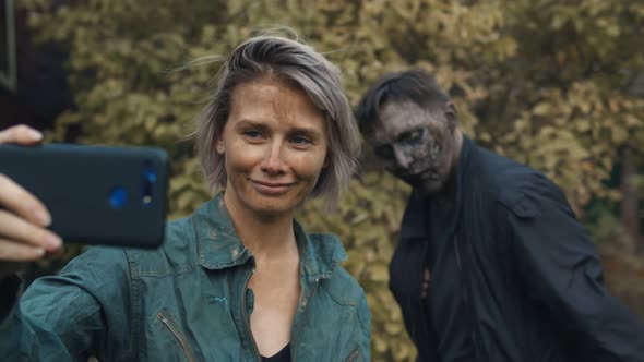 Young Woman Taking Selfie with Zombie on Smartphone Outdoors