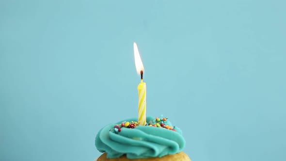 Birthday greetings concept. Blow out candle on muffin, cupcake. Blue background