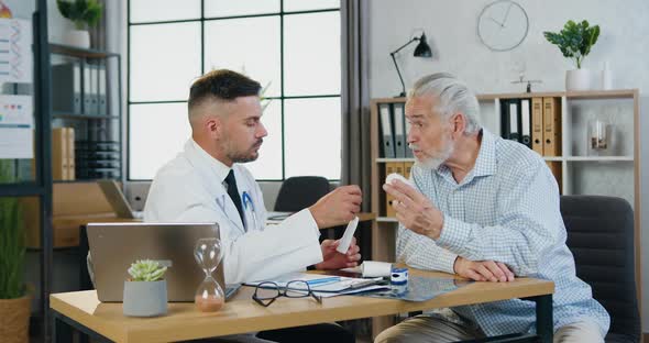 Male Worker Speaking with Old Man, Giving Pills and Explaining Treatment During Medical Visit