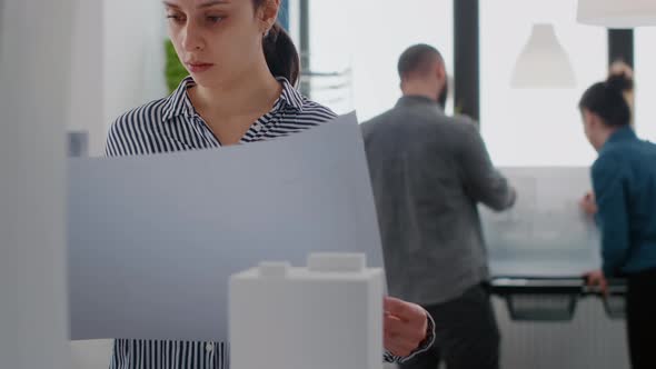 Portrait of Architect Analyzing Blueprints Plan to Work on Construction Layout with Building Model