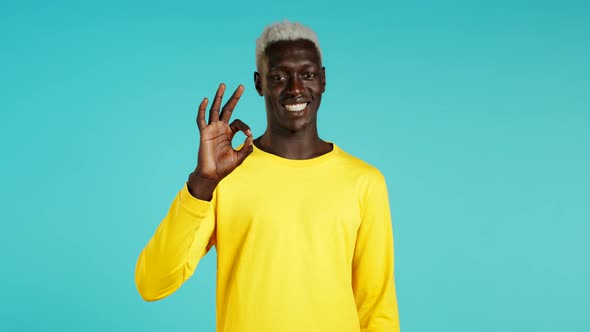 Handsome Young Black African Man Smiles To Camera. Guy Showing OK Sign Over Blue Background. Winner