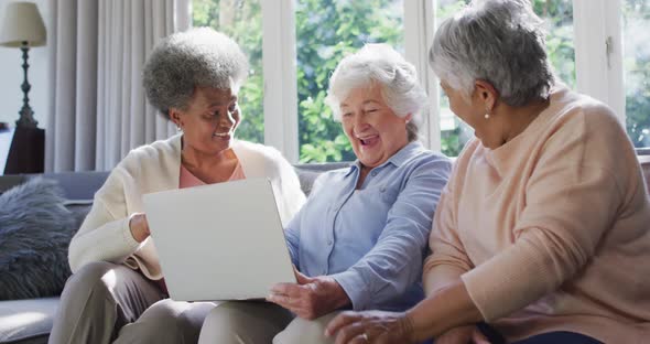 Three diverse senior women using laptop together sitting on the couch at at home