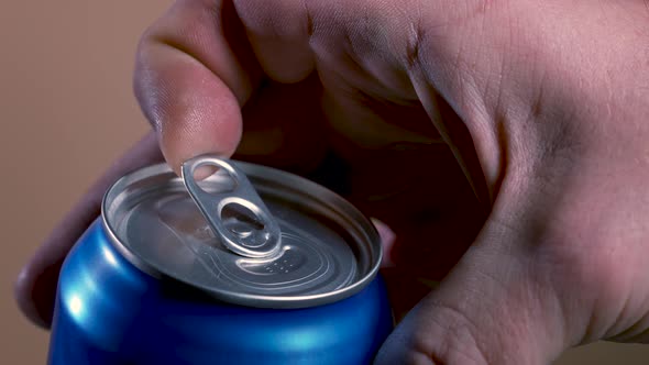 Opening a Shaken Blue Can of Beer From Which a Frothy Drink is Poured