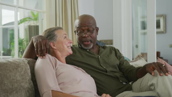 Happy senior diverse couple wearing shirts and watching tv in living room