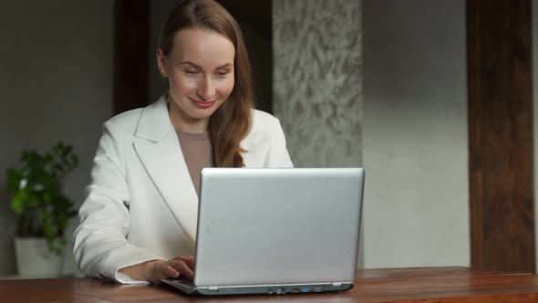 An Excited Business Woman in a White Jacket Celebrates Success in the Workplace By Raising Her Hands