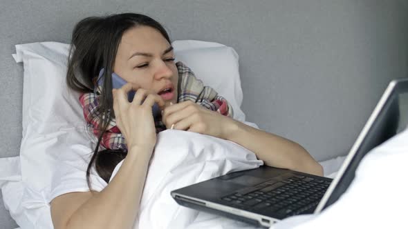 Sick Woman Lying in Bed with Laptop Computer and Smartphone in Self Isolation