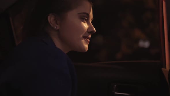 Closeup View of Happy Beautiful Girl Riding in a Taxi at Night Sitting on the Backseat and Looking