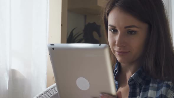 Portrait of Beautiful Brunette Is Surfing Web with Tablet Sitting in Home Interior