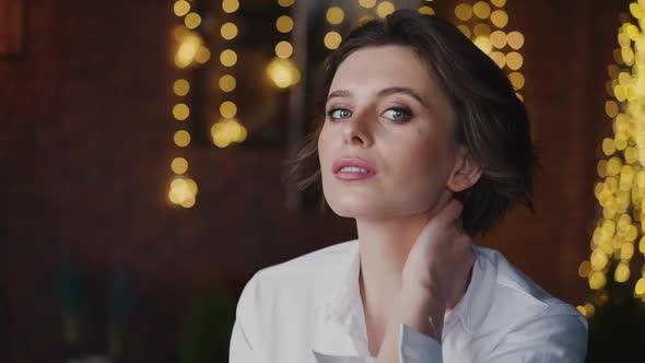 Thoughtful Woman with Makeup in White Shirt Poses at Camera with Cute Smile