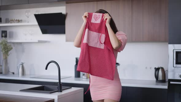 Confident Young Gorgeous Caucasian Woman in Pink Dress Walking in Kitchen Taking Off Apron and