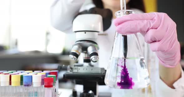 Scientist Holds Transparent Flask with Liquid and Digs Into It Purple Toxin Reagent alt