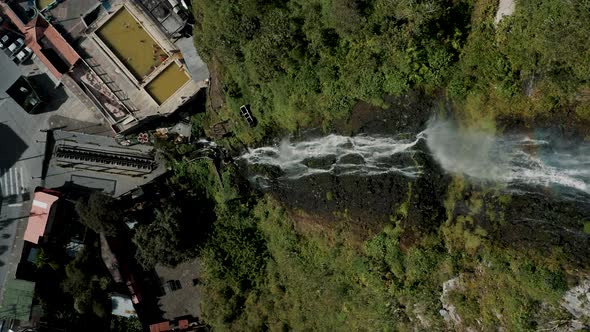 Cascada de la Virgen With Rainbow Flowing Down On Rocky Cliff With Vegetation In Baños de Agua Santa