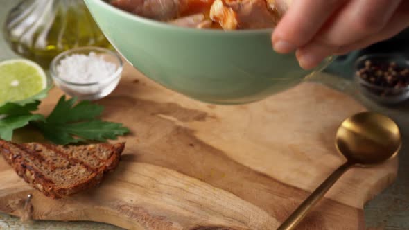 Woman Hand Placing a Plate with Healthy Salmon Fish Soup on Wooden Board