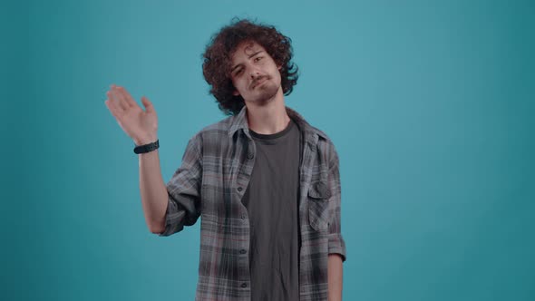 Curly Young Man Who Greets with His Hand Looking Into the Room Finally Smiles