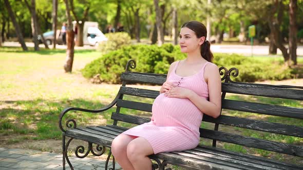 Close Up of Pregnant Woman Hands Stroking Belly on a Park Bench in the Summer