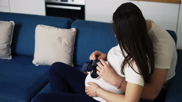 Lovely Pregnant Woman and Her Husband Holding Baby Shoes on Belly