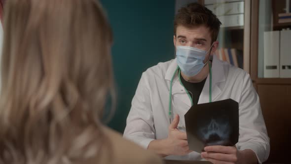 Doctor Wearing Medical Protective Mask Consulting Young Woman Looking at Xray