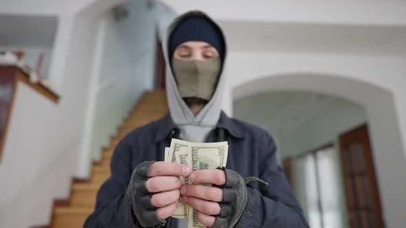 Blurred Burglar in Mask Counting Dollars Standing in Wealthy House Indoors