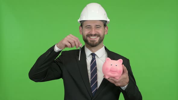 Happy Engineer Holding Piggy Bank with House Key Against Chroma Key