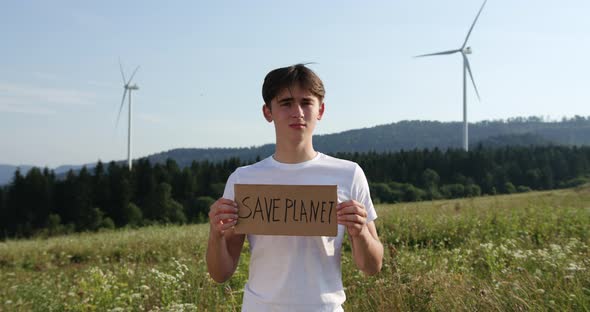 Outdoor of Men Activist with Save the Planet Ecology Poster. In Background Forest and Wind Turbine