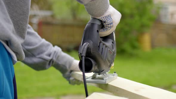 Close Up Unrecognizable Worker in Nature Sawing Board with Electric Jigsaw