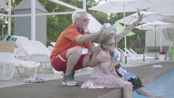 Happy Mature Couple on the Edge of the Pool Hugging Little Granddaughter