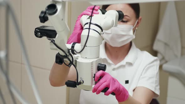 A Female Endodontist Is Treating Canals Under the Microscope.