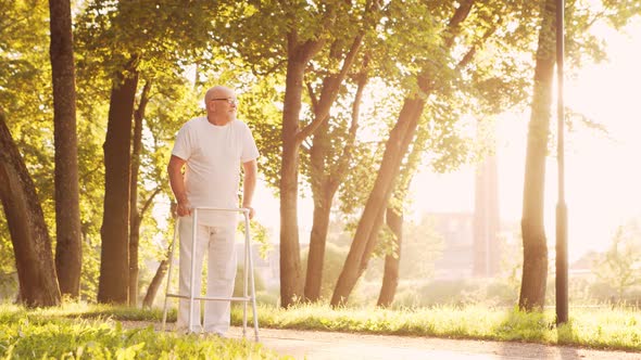 Disabled old man is walking with a walker. Handicapped patient in the park.