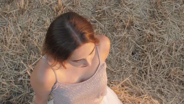 beautiful girl with long hair sitting lean on a haystack in field at sunset,young woman