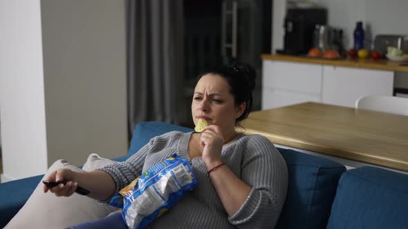 Overweight Woman Sitting on Couch at Home Watching Tv and Eating Potato Chips