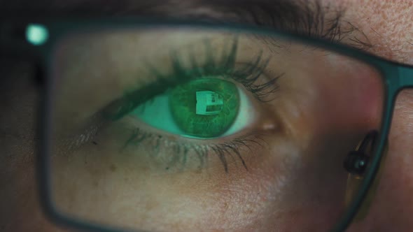 Macro shot of a girl's eye with glasses looking at a computer screen.