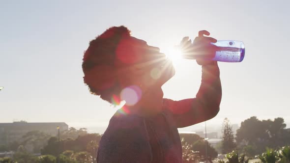 Fit african american man exercising outdoors in city, resting and drinking from water bottle