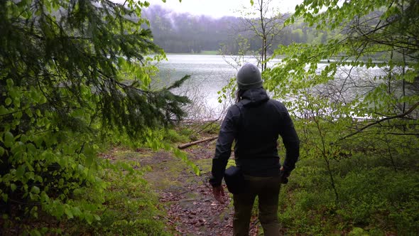 Man Walking In Deep Forest. Young man whit a gray hat walking in the pine forest and mountain lake.