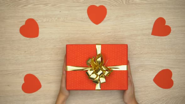 Woman Putting Gift Box on Wooden Table Covered With Confetti, Top View