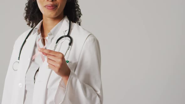 Video of smiling biracial female doctor holding pink breast cancer ribbon