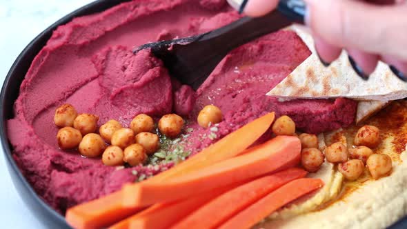 Beetroot hummus and classic hummus in black dish with carrots and pita bread. 