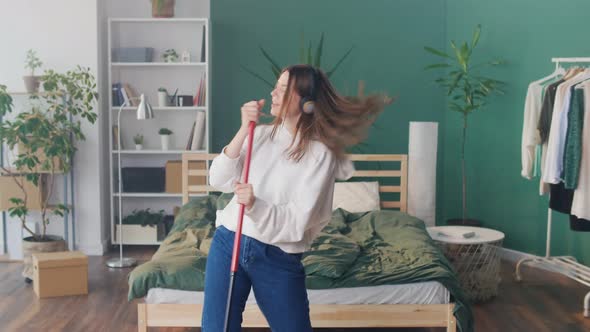 Happy Young Girl Student in Headphones Dances and Sings Has Fun in a Cozy Room