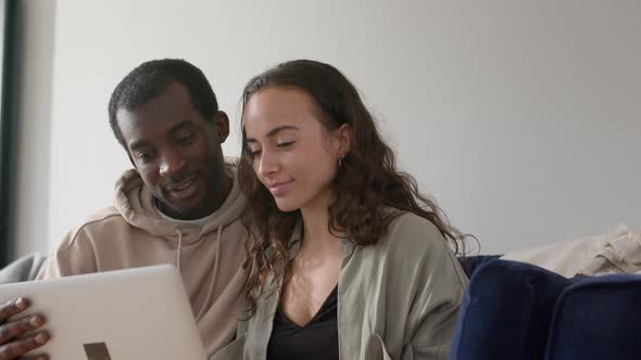 Relaxed Young Couple At Home Sitting On Sofa Browsing Internet On Laptop Computer