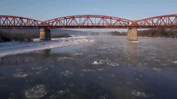 Drone Shot Flies Forward Over the Frozen River and Under the Red Steel Bridge Aerial  Footage