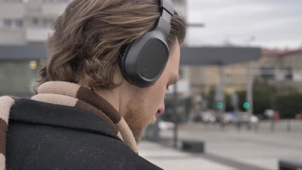 stylish guy in scarf and coat listen a music on streaming service by using mobile phone